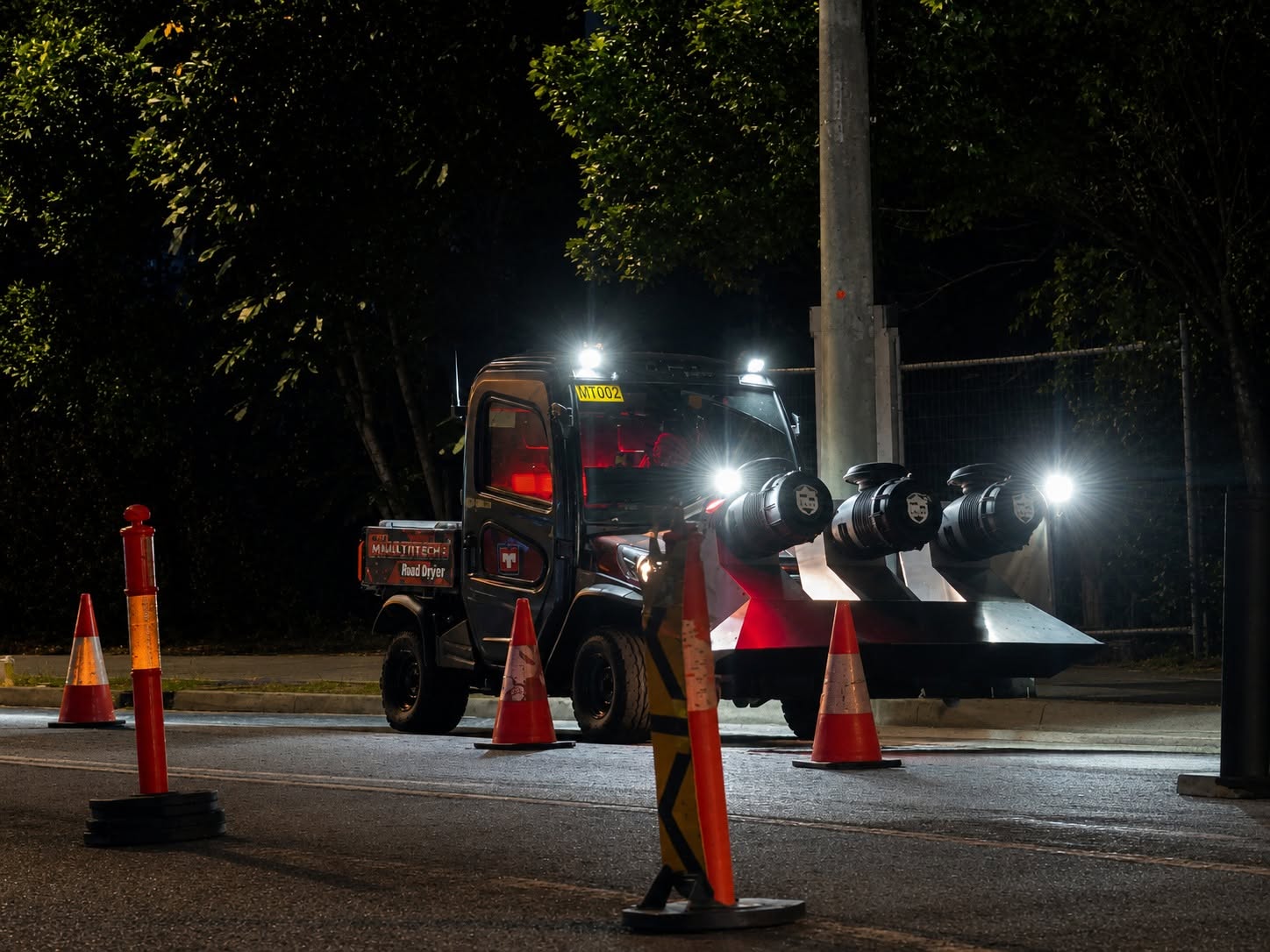 Multitech road dryer working a coned-off road at night with its three jets lit